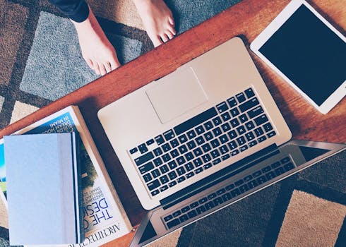 Top view of a cozy home workspace featuring a laptop, tablet, and books on a wooden table.