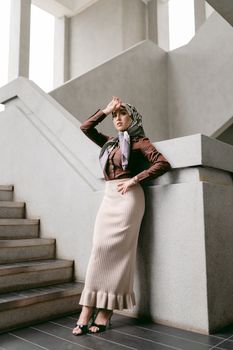 Stylish woman in hijab poses elegantly on stairs in Kuala Lumpur.
