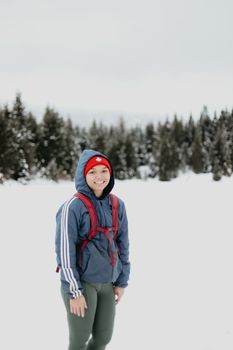 A woman in winter gear smiling while hiking through a snowy forest landscape.