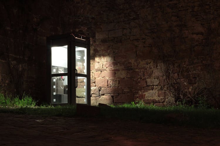 Telephone Booth Beside Brown Wall During Nighttime