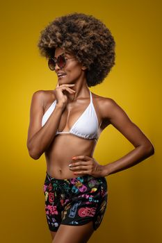 Fashionable woman with afro hair posing confidently in a studio against a vibrant yellow background.
