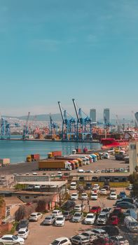 A busy day at the İzmir harbor showcasing cargo ships, cranes, and vehicles in an urban setting.