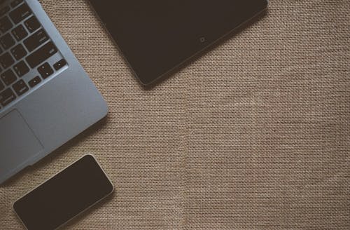 Black Ipad Near Macbook on Brown Textile