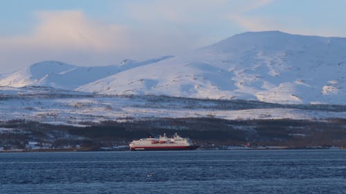 Passenger Ship Sailing along Snowed Mountain Coastline