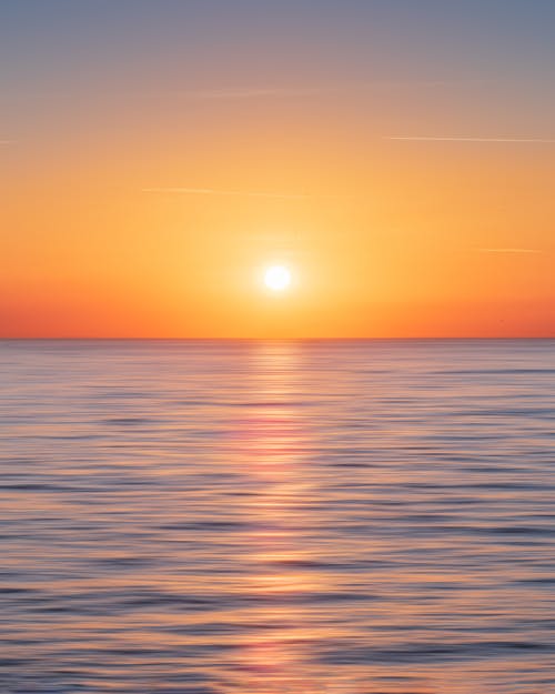 平靜的水與太陽和橙色的天空