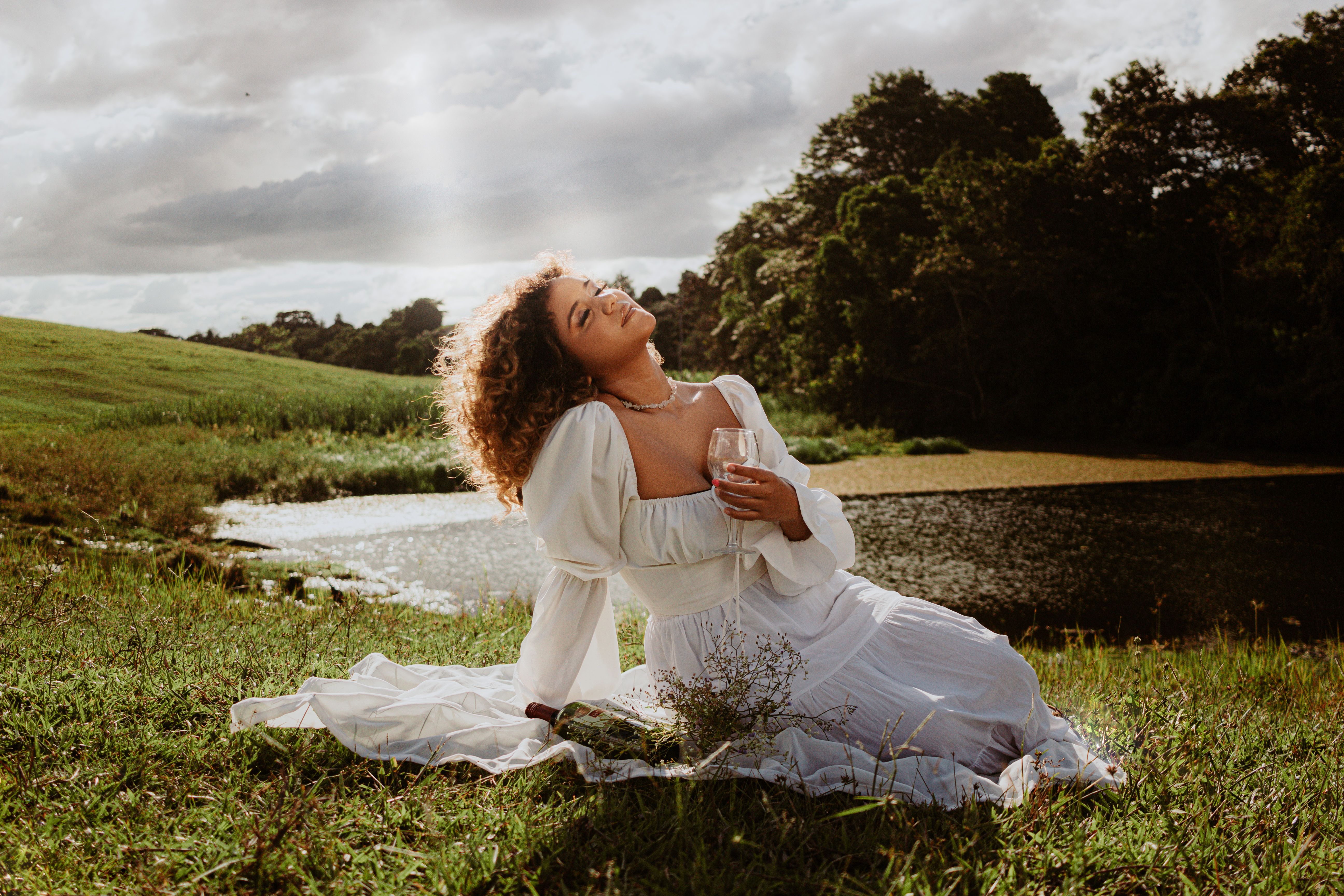 Young Woman in a White Dress Sitting on a Field and Holding a Glass of ...