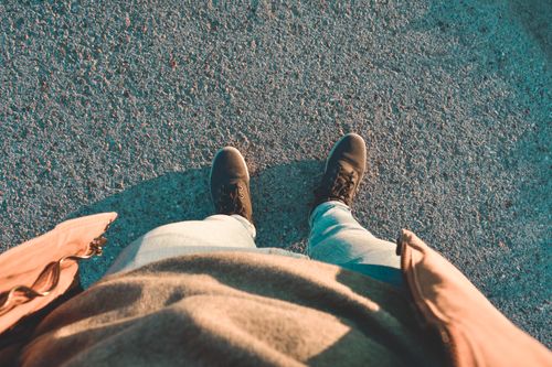 Free View from above of a person in casual attire and boots on a sunlit street during summer. Stock Photo
