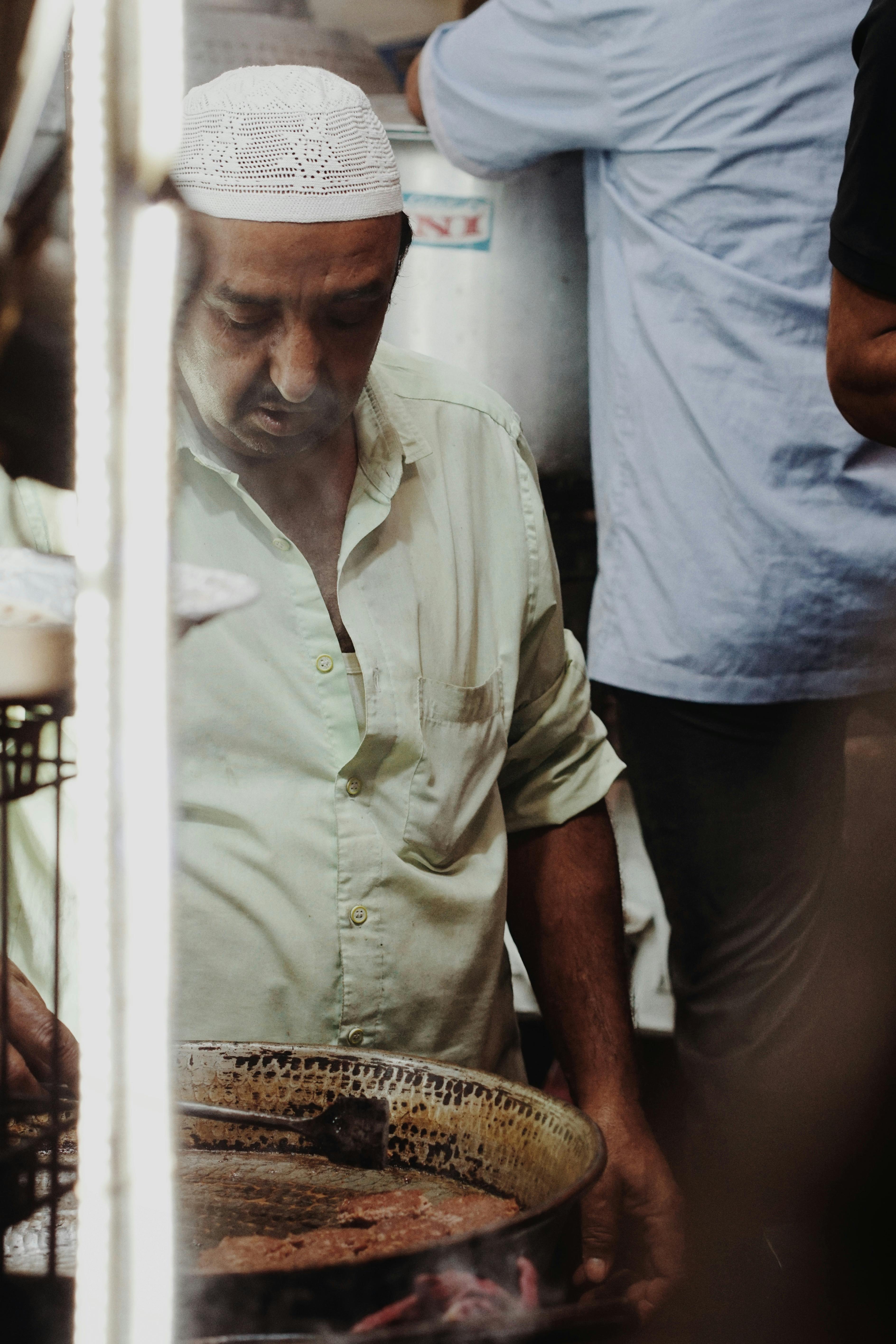A man wearing a traditional hat cooks food at a bustling market in India.