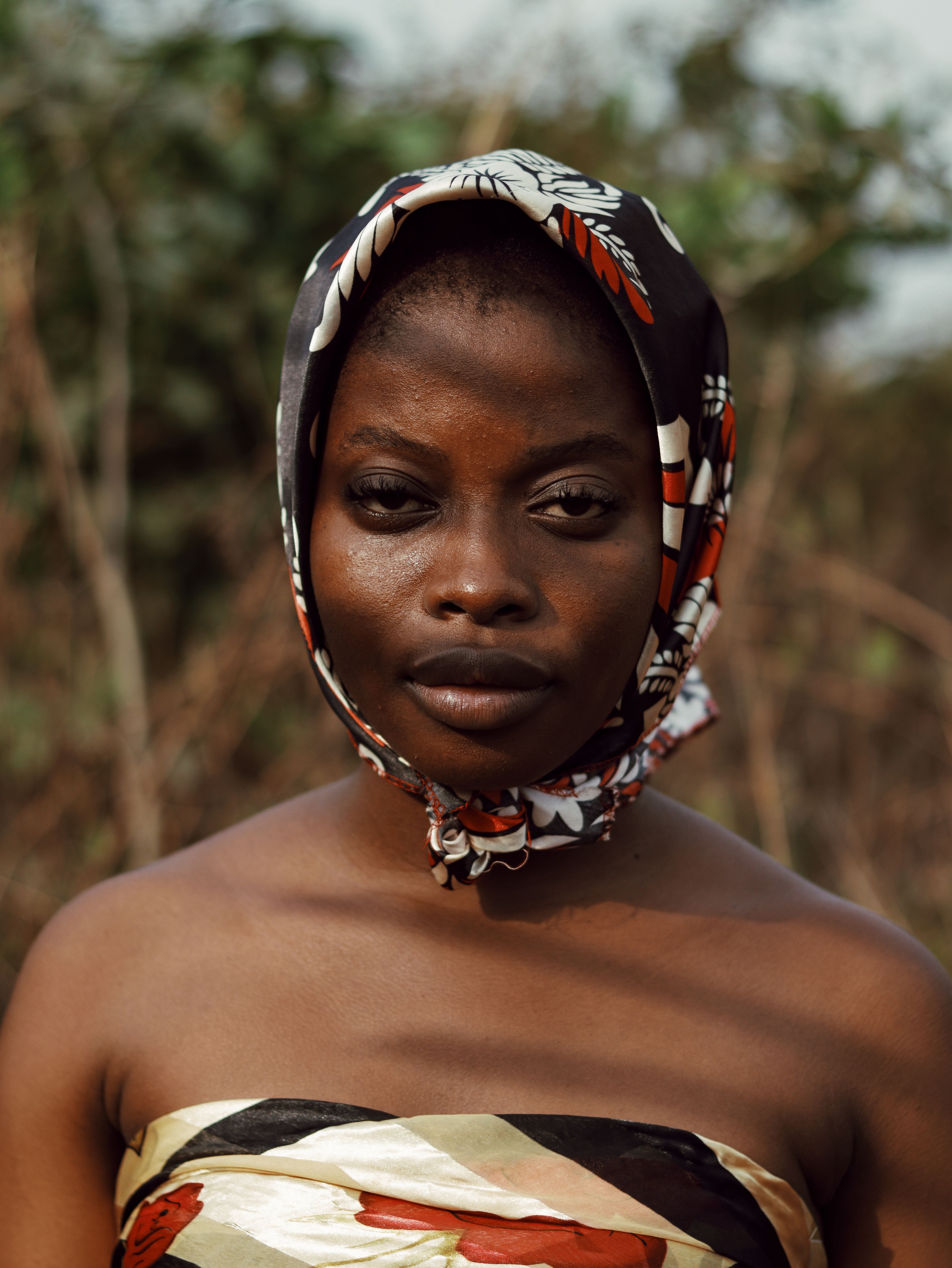 A striking portrait of a woman with a floral scarf in a natural outdoor setting.