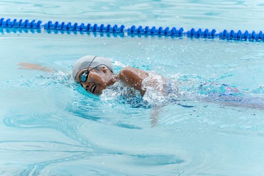 Focused female swimmer practicing freestyle in a swimming pool with swim cap and goggles.