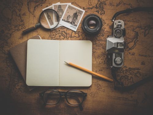 Free A flat lay of travel essentials on a vintage map surface, including a camera, notebook, and magnifying glass. Stock Photo