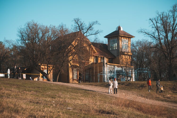 People Walking On Hill Near Old Mansion 