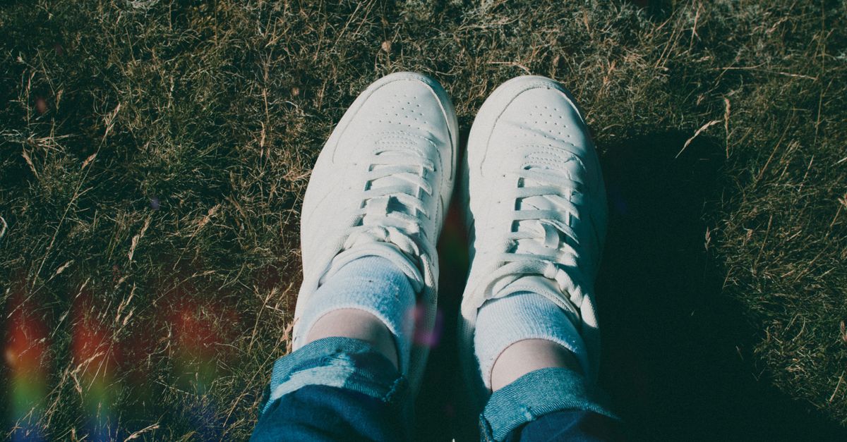 Top view of white sneakers and jeans on grassy field, natural sunlight.