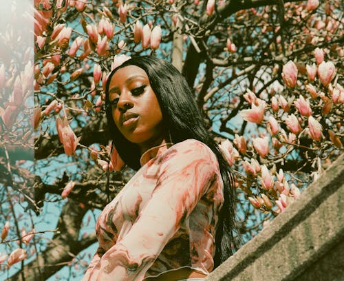 A woman in pink top and black pants standing next to a tree