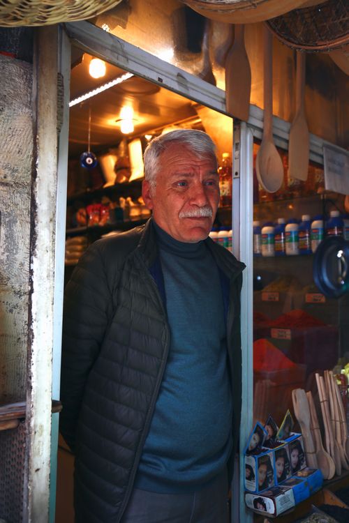 Free Senior man with a mustache stands at shop entrance, surrounded by goods. Stock Photo