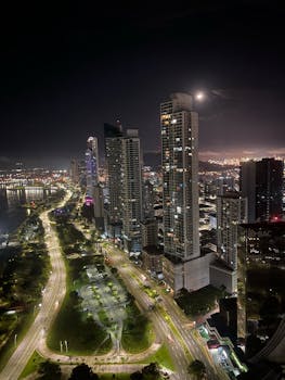 A breathtaking aerial view of a modern city skyline at night, featuring illuminated skyscrapers along a waterfront.