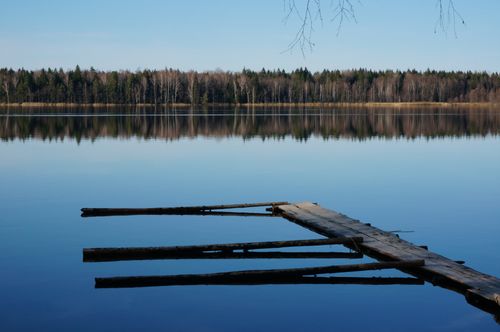 Free Tranquil lake scene with a wooden pier and forest reflection in Minsk Region, Belarus. Stock Photo