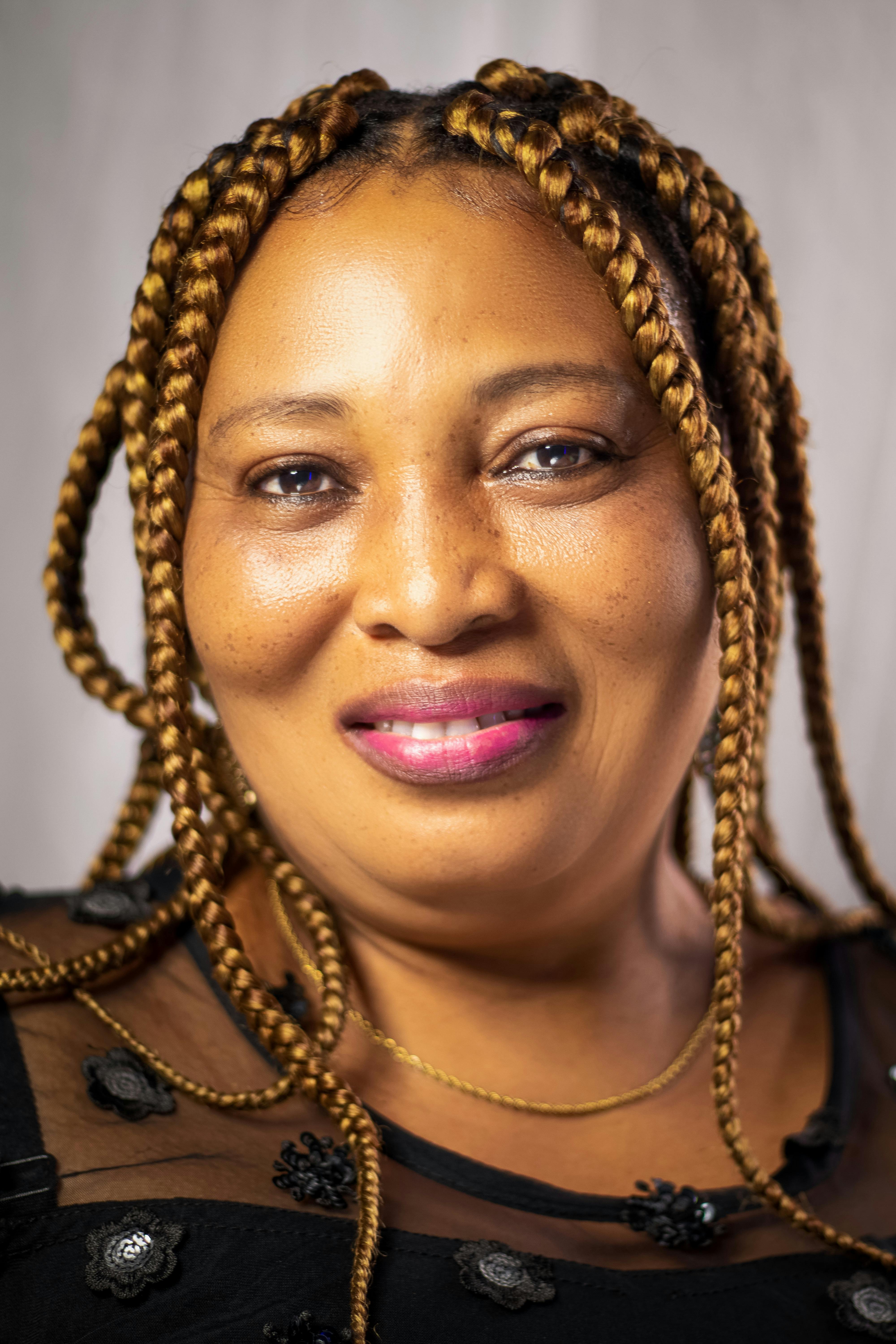 Portrait of a smiling woman with braided hair and pink lips in a studio setting.