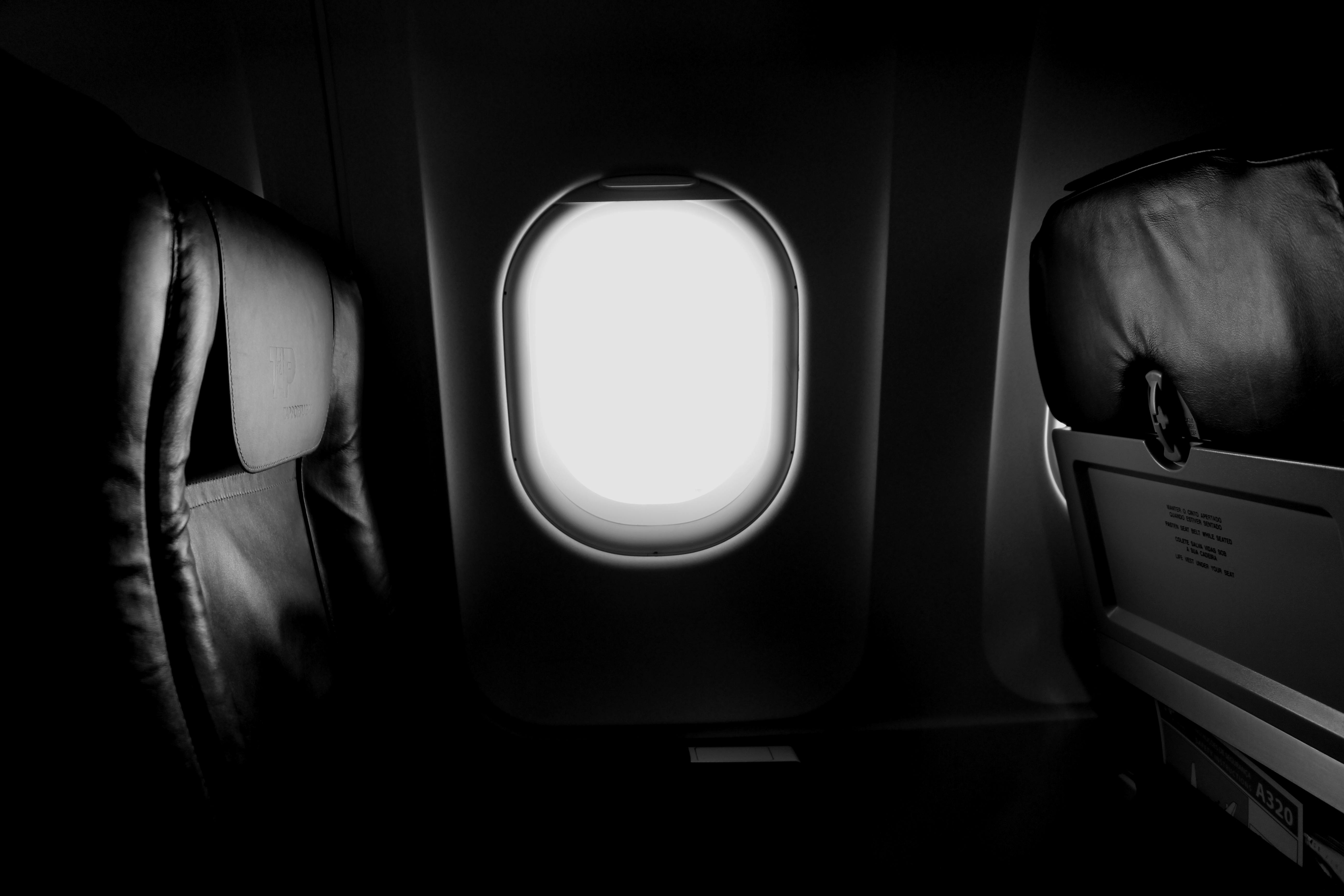 grayscale of airplane window and chair