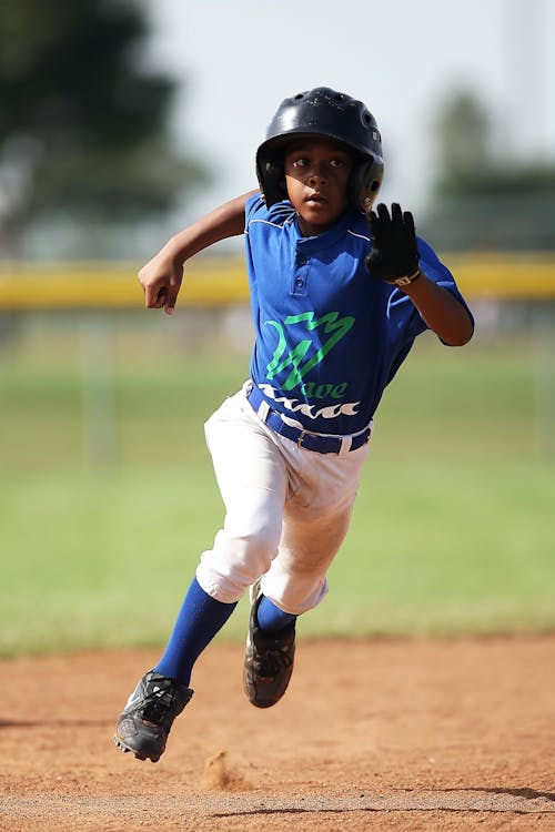 Junge Im Blauen Und Weißen Baseballtrikot, Das Tagsüber Auf Feld Des Braunen Bodens Läuft