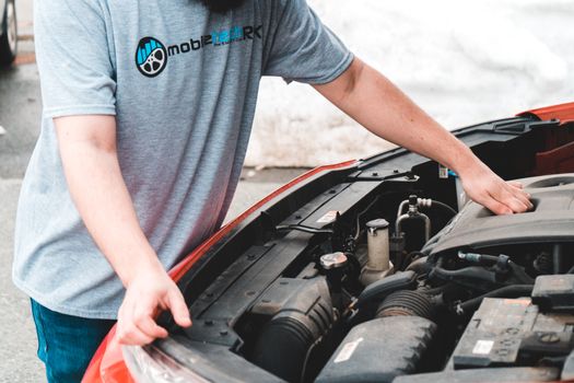 A man inspects the engine of a car, likely addressing an emergency breakdown.