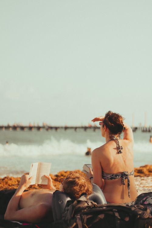 Free A serene beach scene with a couple enjoying reading and sunbathing by the sea. Stock Photo