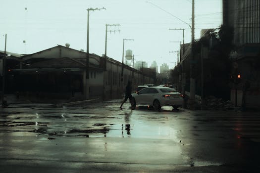 A moody urban street with rain puddles and a person crossing, captured on a rainy day.