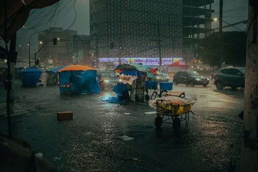 Rain-soaked urban street with market stalls under umbrellas during a thunderstorm.