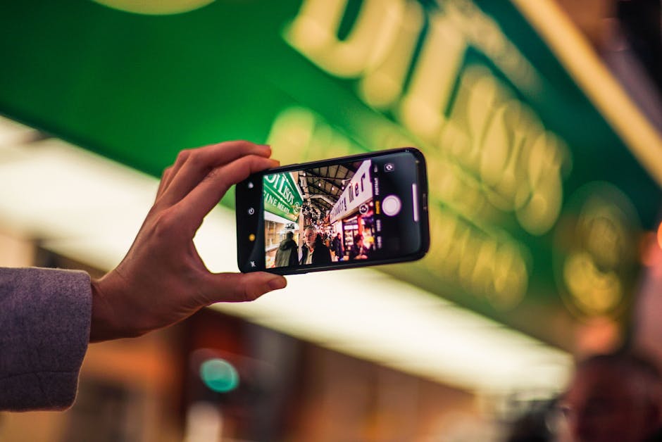 A person takes a vibrant city street photo with a smartphone at night, showcasing technology's role in modern photography.