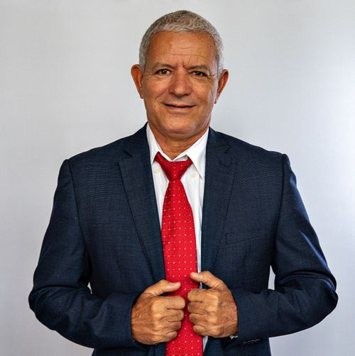 Free Senior businessman smiling confidently in a suit and red tie against a gray background. Stock Photo