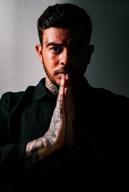 Free Dark portrait of a tattooed man with prayer hands, creating a dramatic shadow effect. Stock Photo