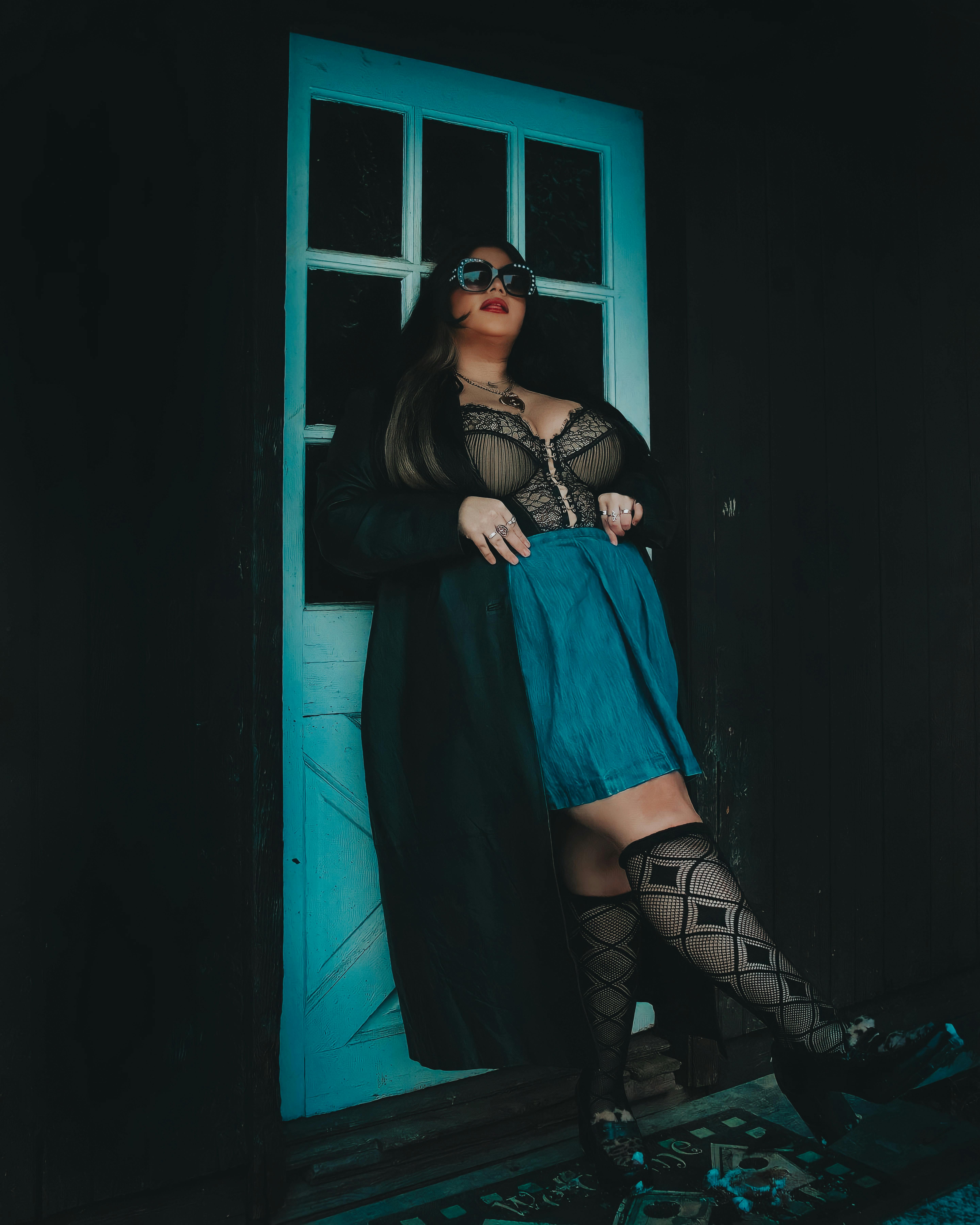 Free A fashionable woman posing against a blue door in trendy attire and sunglasses. Stock Photo