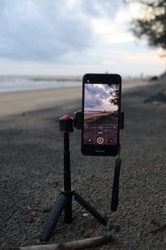 Smartphone mounted on a tripod capturing a serene beach sunset, showcasing technology in nature.
