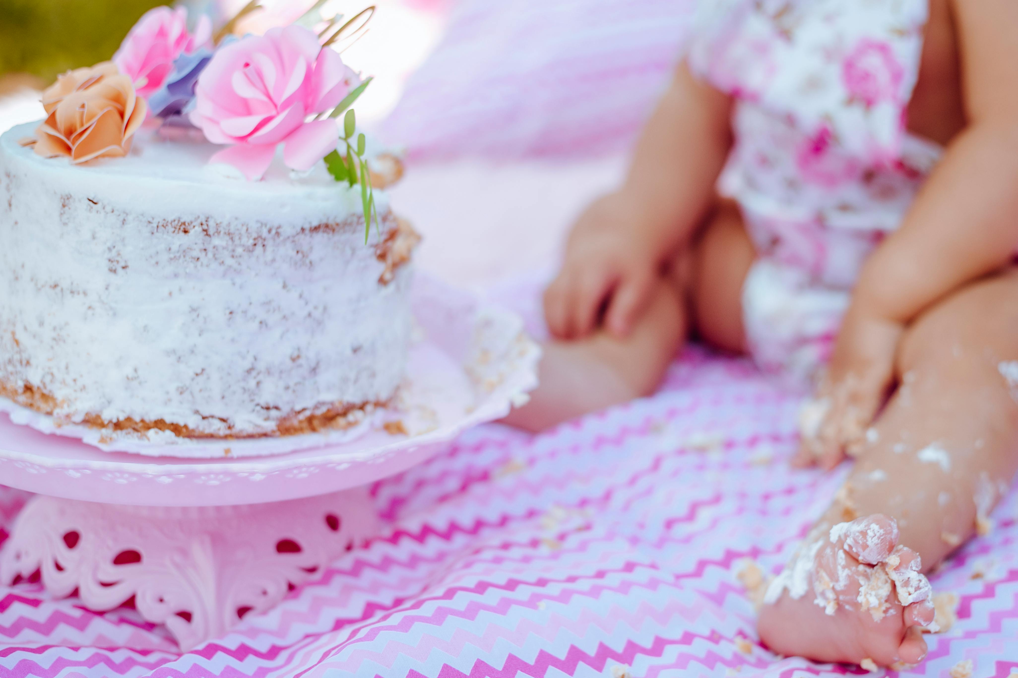 A baby enjoys a cake smash on a patterned blanket, celebrating a special day.