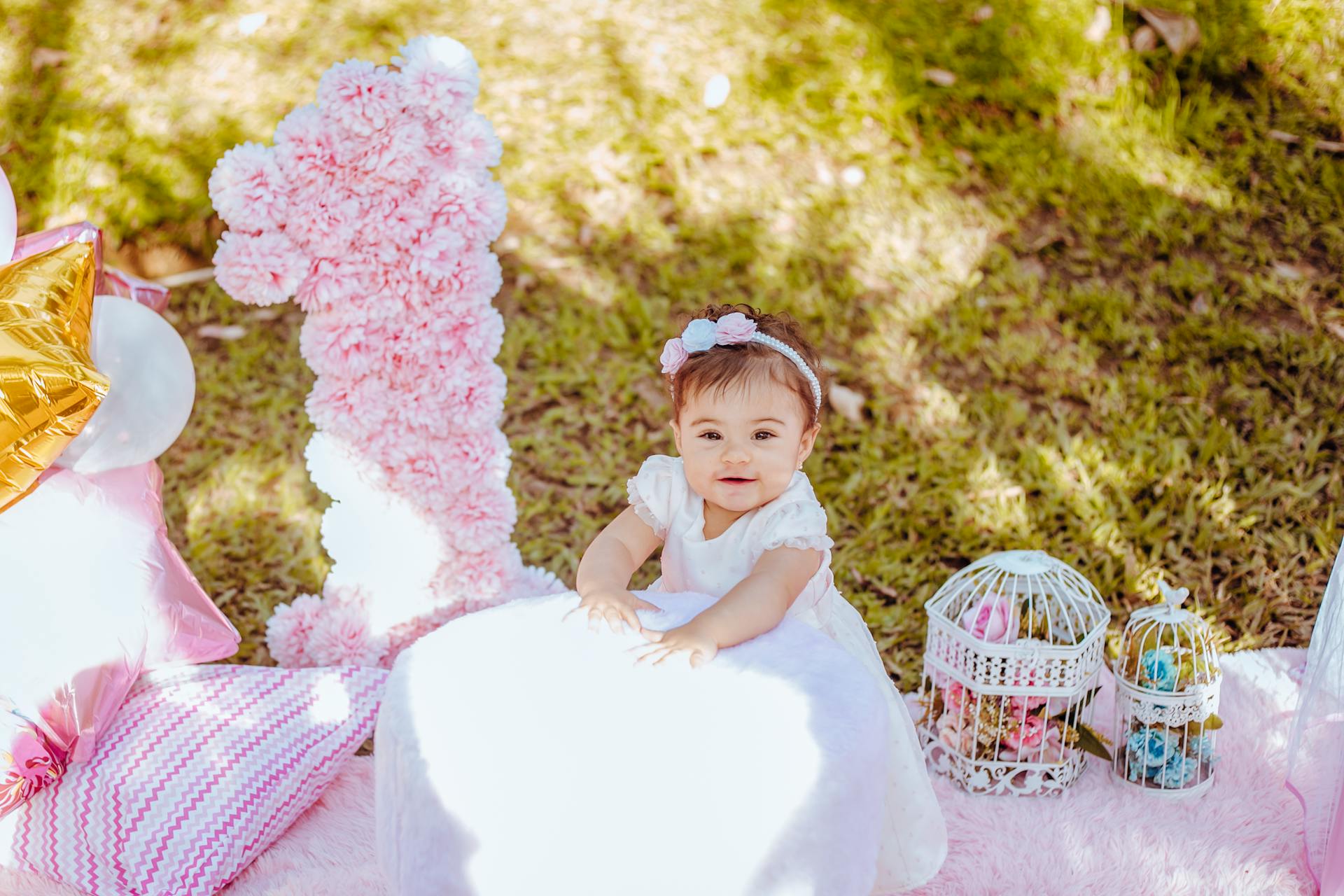 Cute baby enjoying an outdoor birthday picnic with decorations and balloons.