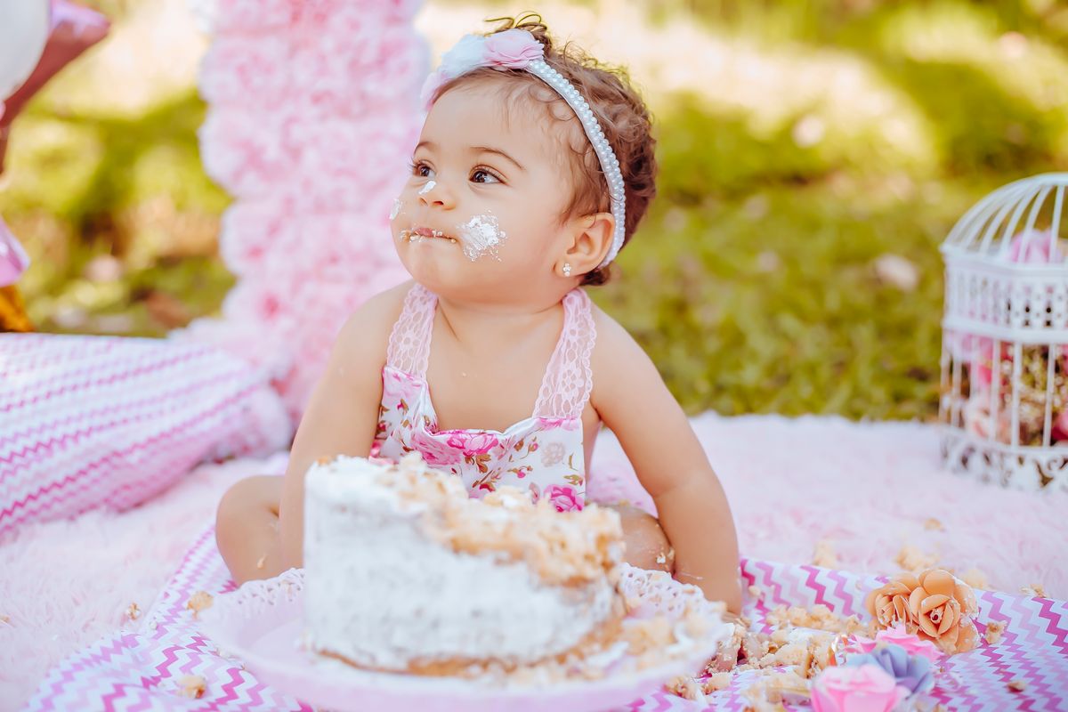 Charming scene of a baby's first cake smash outdoors with a pastel theme and floral decor. Stock Photo.