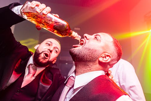 Man Pouring Alcohol to other Man Mouth