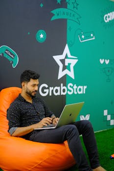 Adult man with a beard focused on his laptop in a vibrant creative workspace with GrabStar theme.