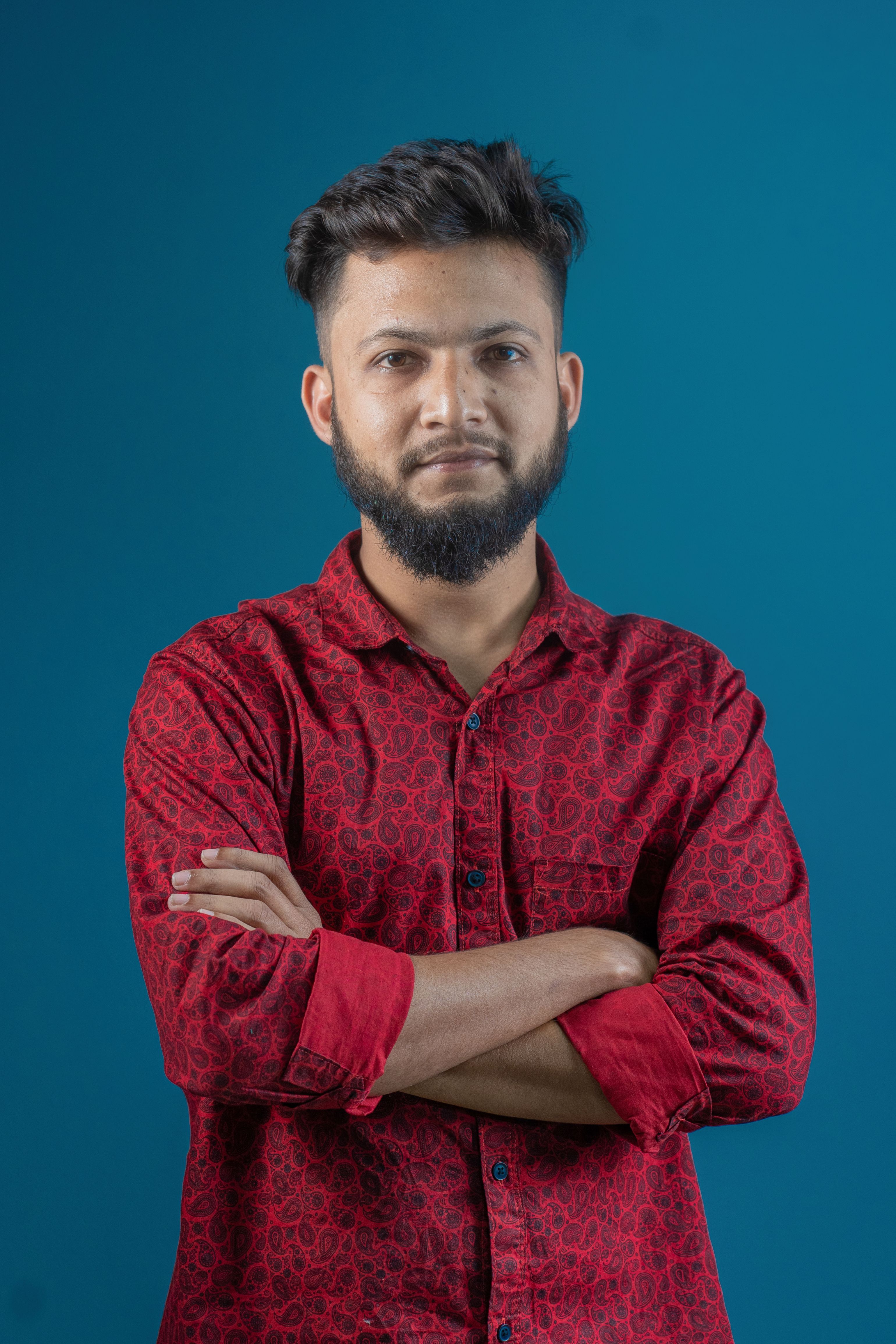 Portrait of a confident man with a beard in a red shirt against a solid blue background.