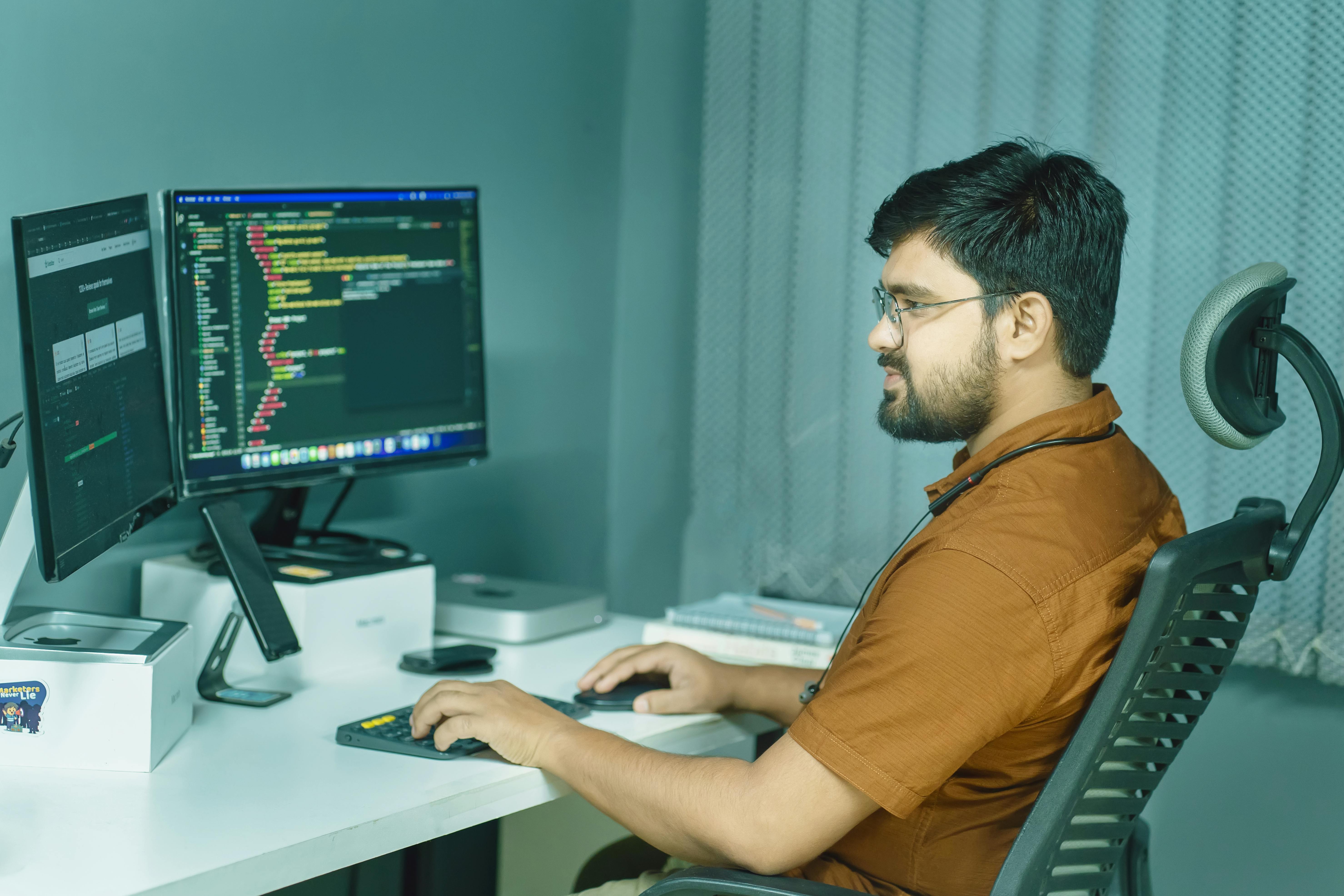 a man sitting at a desk with two monitors