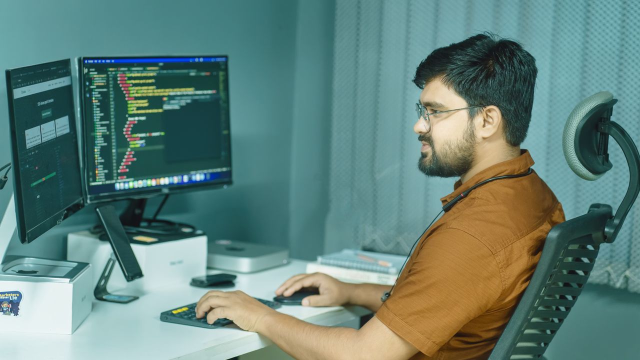 A focused developer coding at a modern office with dual monitors, showcasing a tech-driven workspace.