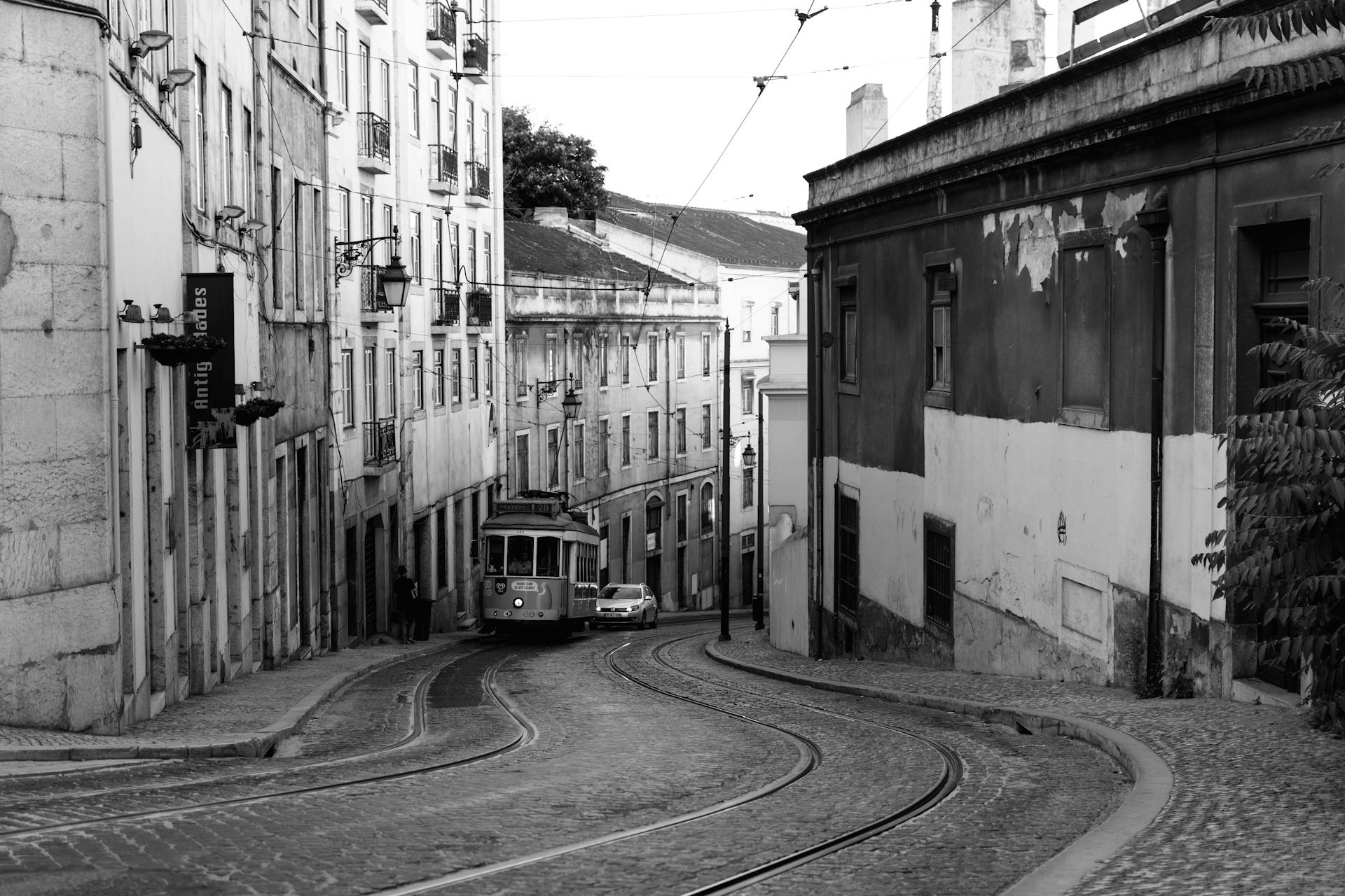 Black and white photo of a vintage tram navigating narrow Lisbon streets, highlighting urban charm.