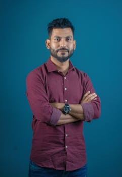 A confident man in a casual red shirt poses against a turquoise background, embodying modern style.