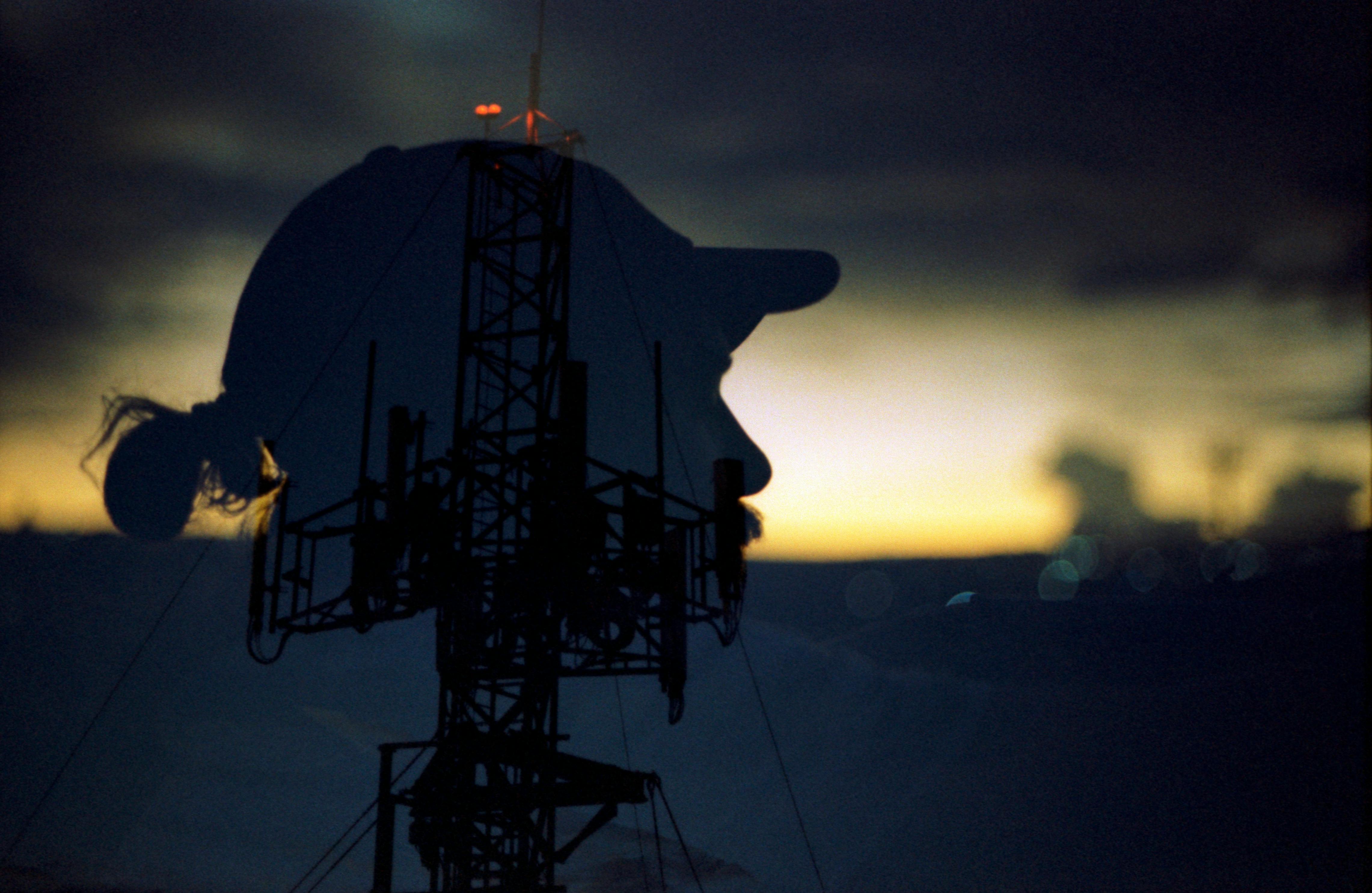 Creative double exposure of a woman's silhouette with a communications tower at sunset.