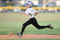 镜头中，一名年轻的棒球运动员身穿制服和头盔，在球场上快速奔跑