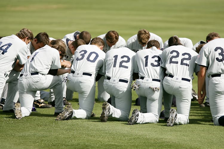 Baseball Player Kneeling On Grass Field During Daytime