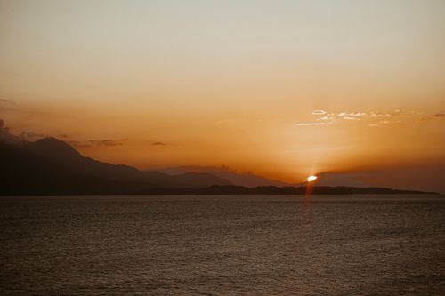 Free A breathtaking view of a mountainous coastline silhouetted against a vivid sunset sky. Stock Photo