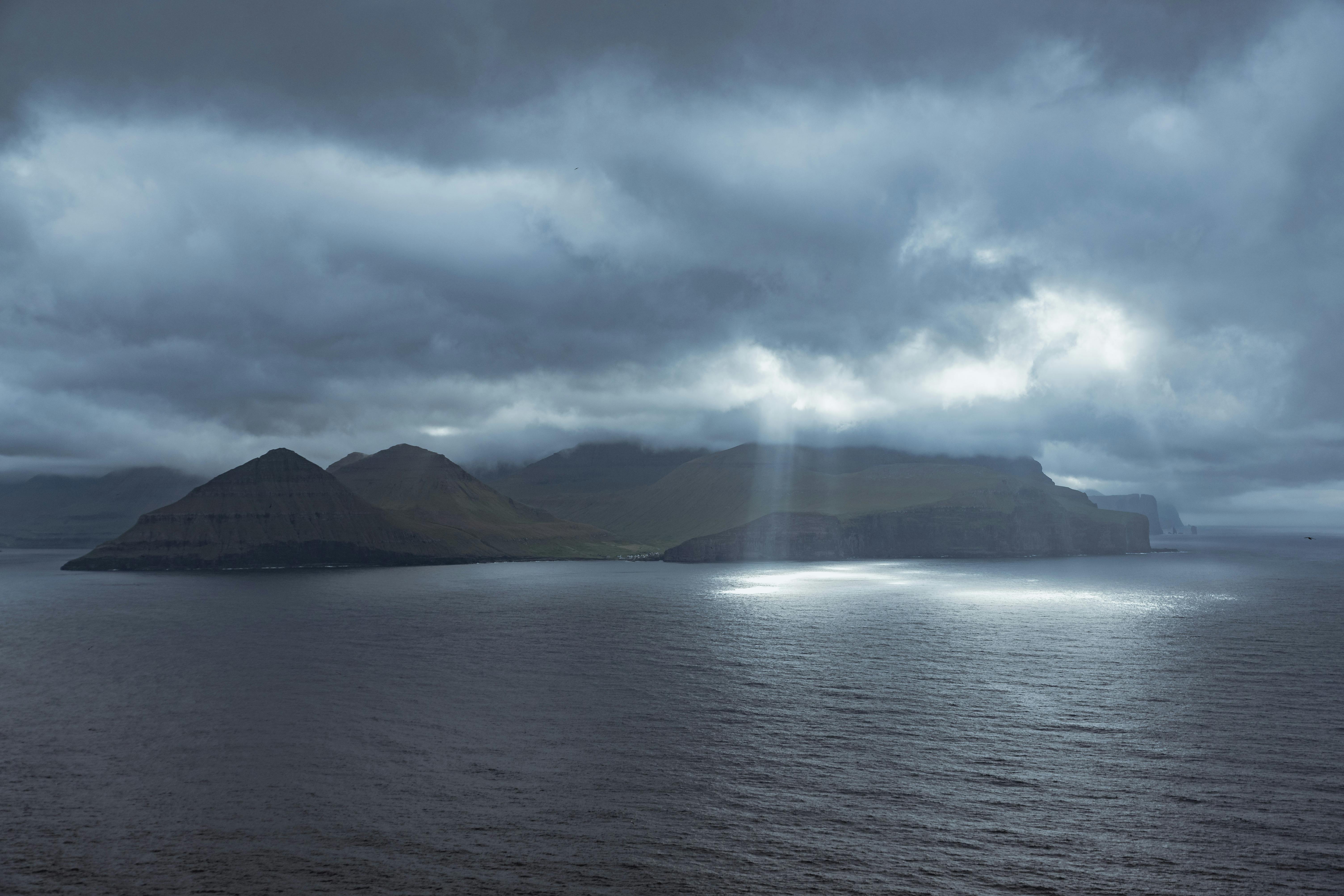 A stunning view of the Faroe Islands with dramatic clouds and sunlight peeking through.