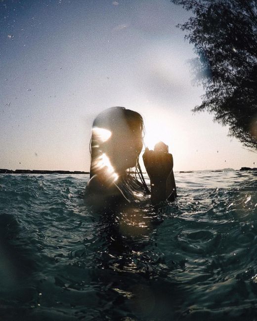 A woman swimming in the ocean at sunset, creating a serene silhouette with backlit water.