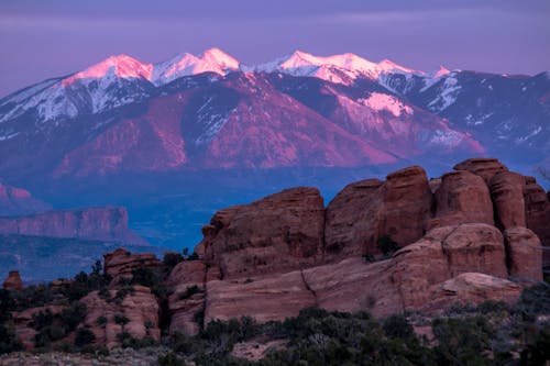 Green Trees and Rock Formation Overlooking Snow Coated Mountain Ranges at Daytime